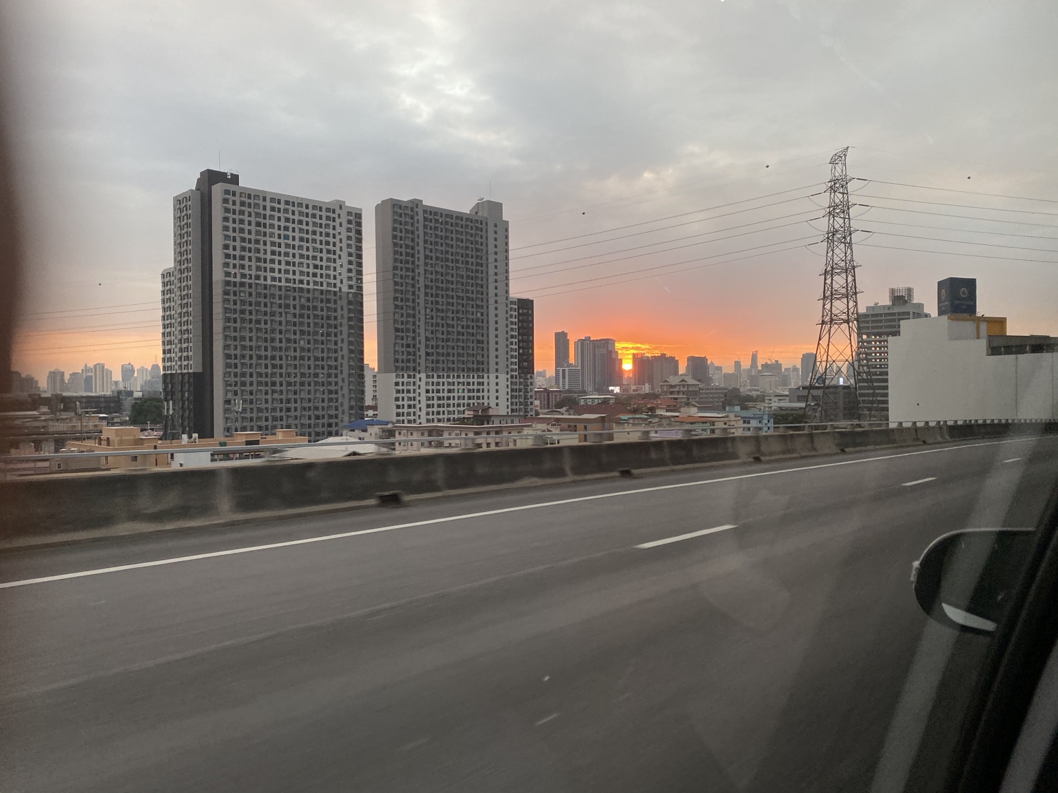 The sun setting between city buildings, photographed from the road.